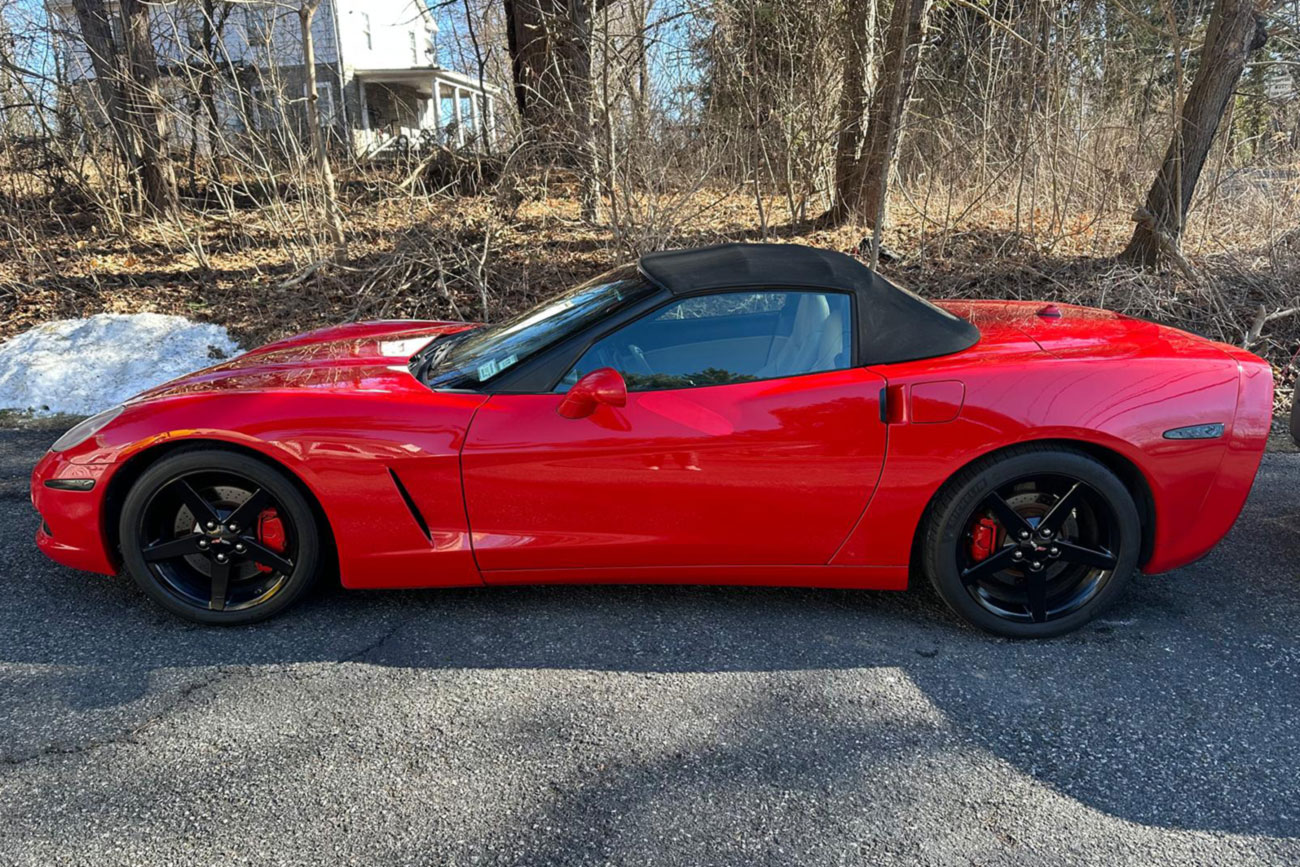 A red Corvette parked on a driveway next to a construction site, with a view of a house in the background.